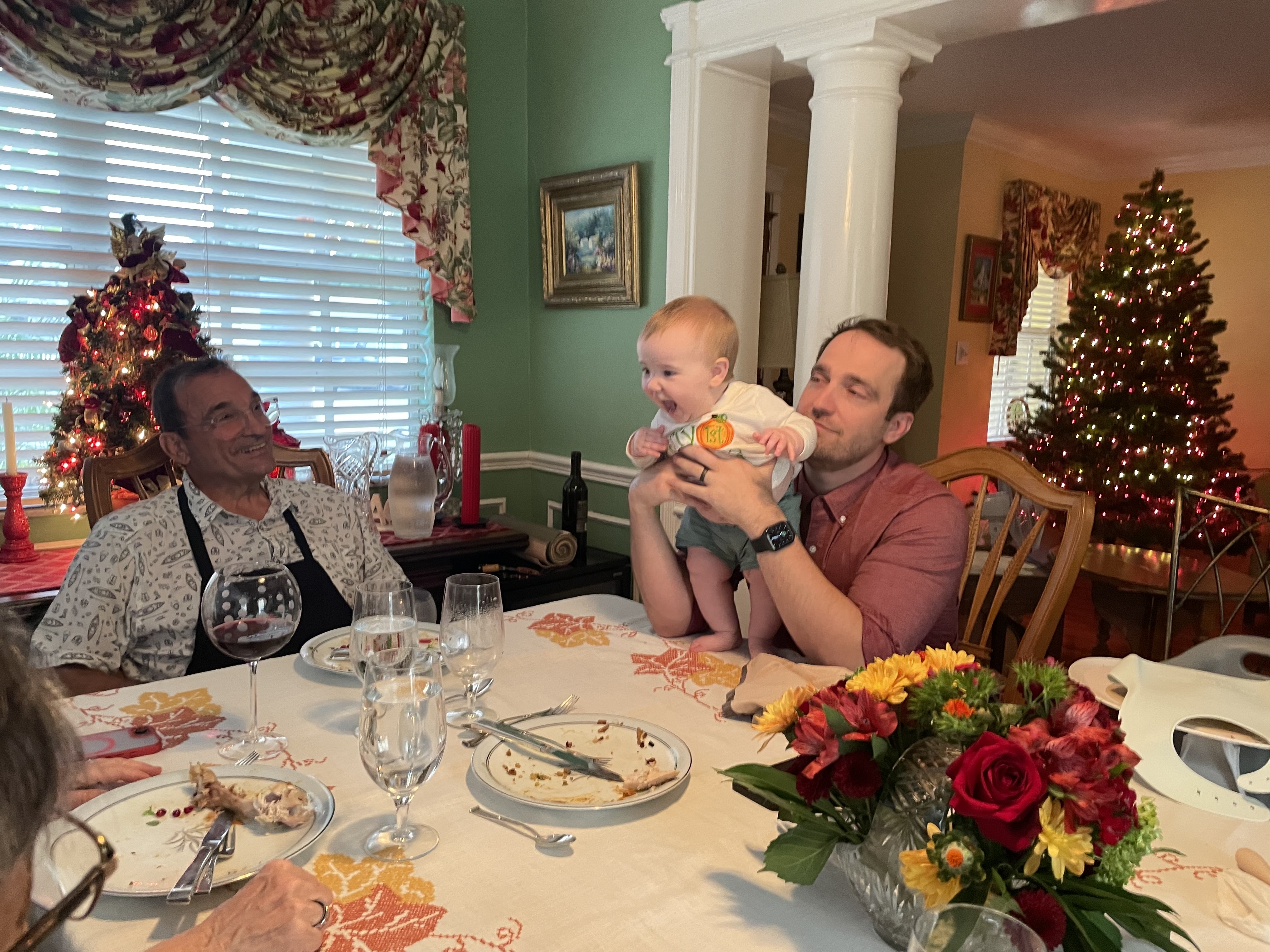 Thanksgiving table after dinner, baby standing on the table with help while family looks on