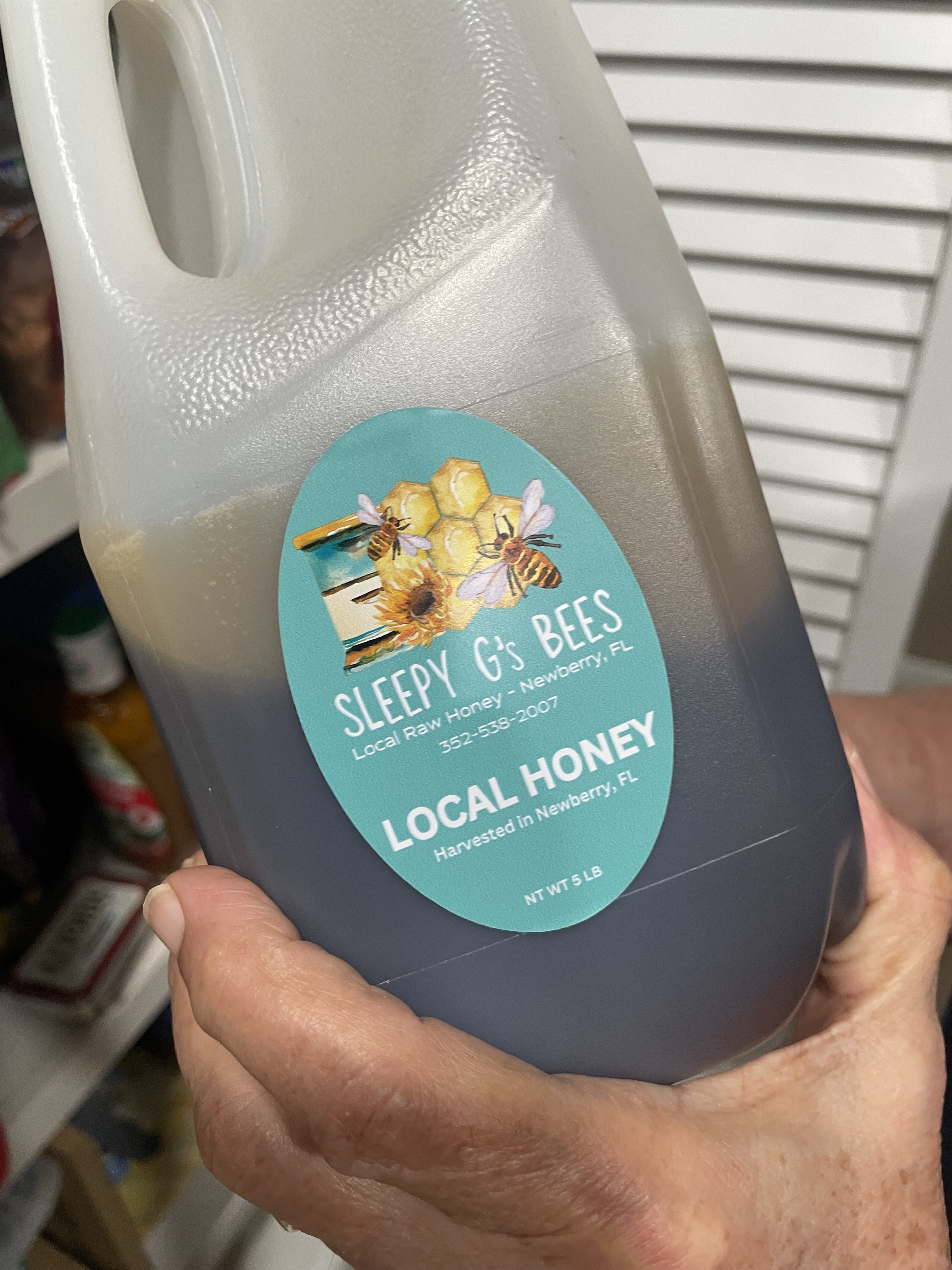 Hand holding a small mason jar of honey from an honor-system stand