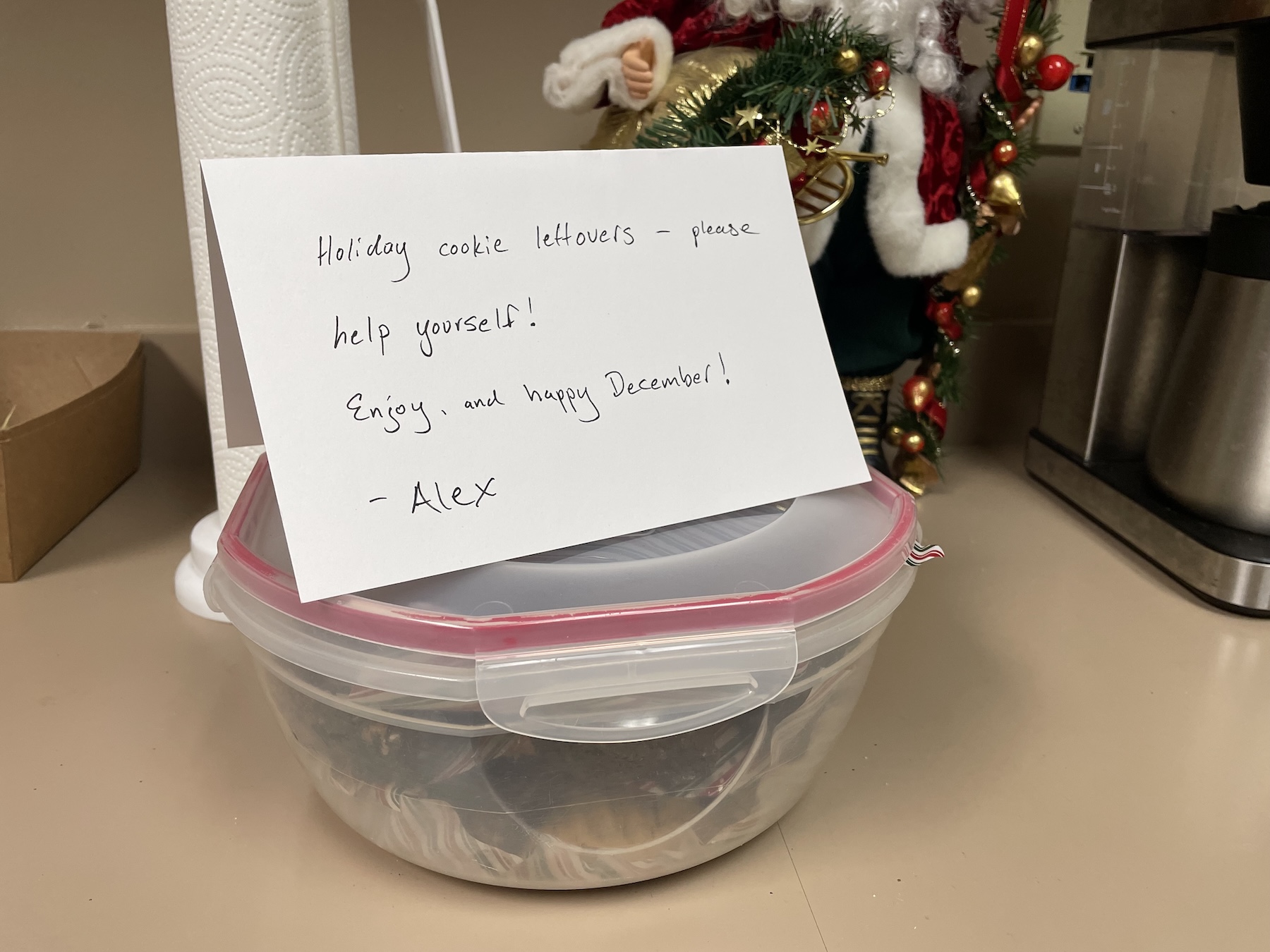 Container of holiday cookies with a handwritten note in an office break room