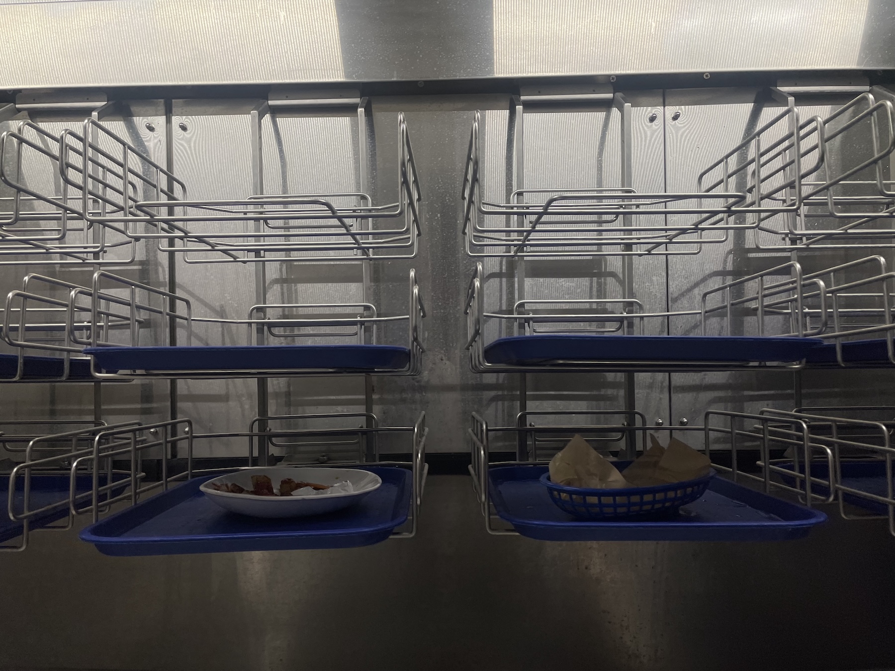 Cafeteria dish conveyor with trays moving through a stainless steel system