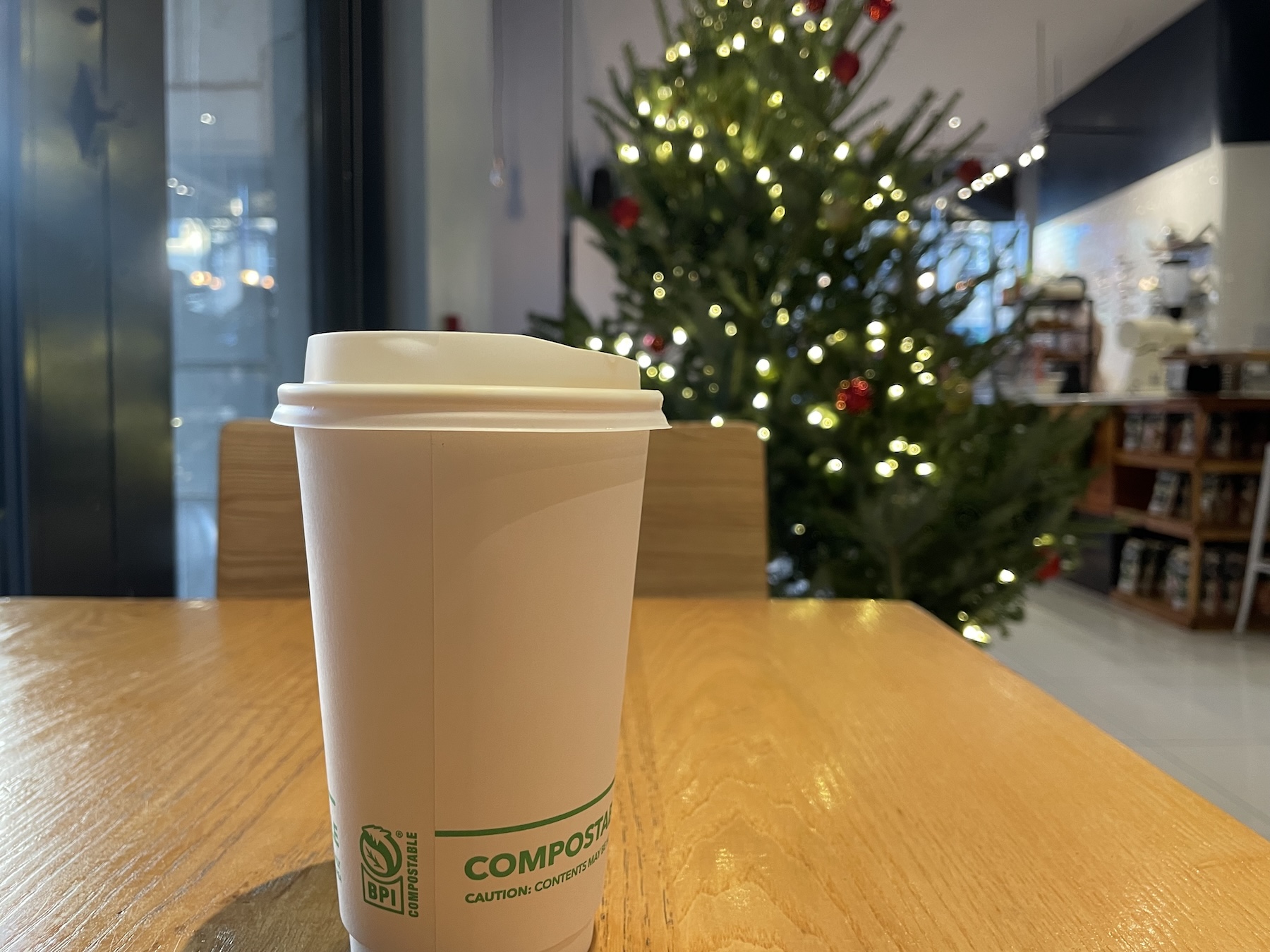 Coffee cup on a wooden table in a quiet coffee shop with a lit Christmas tree in the background