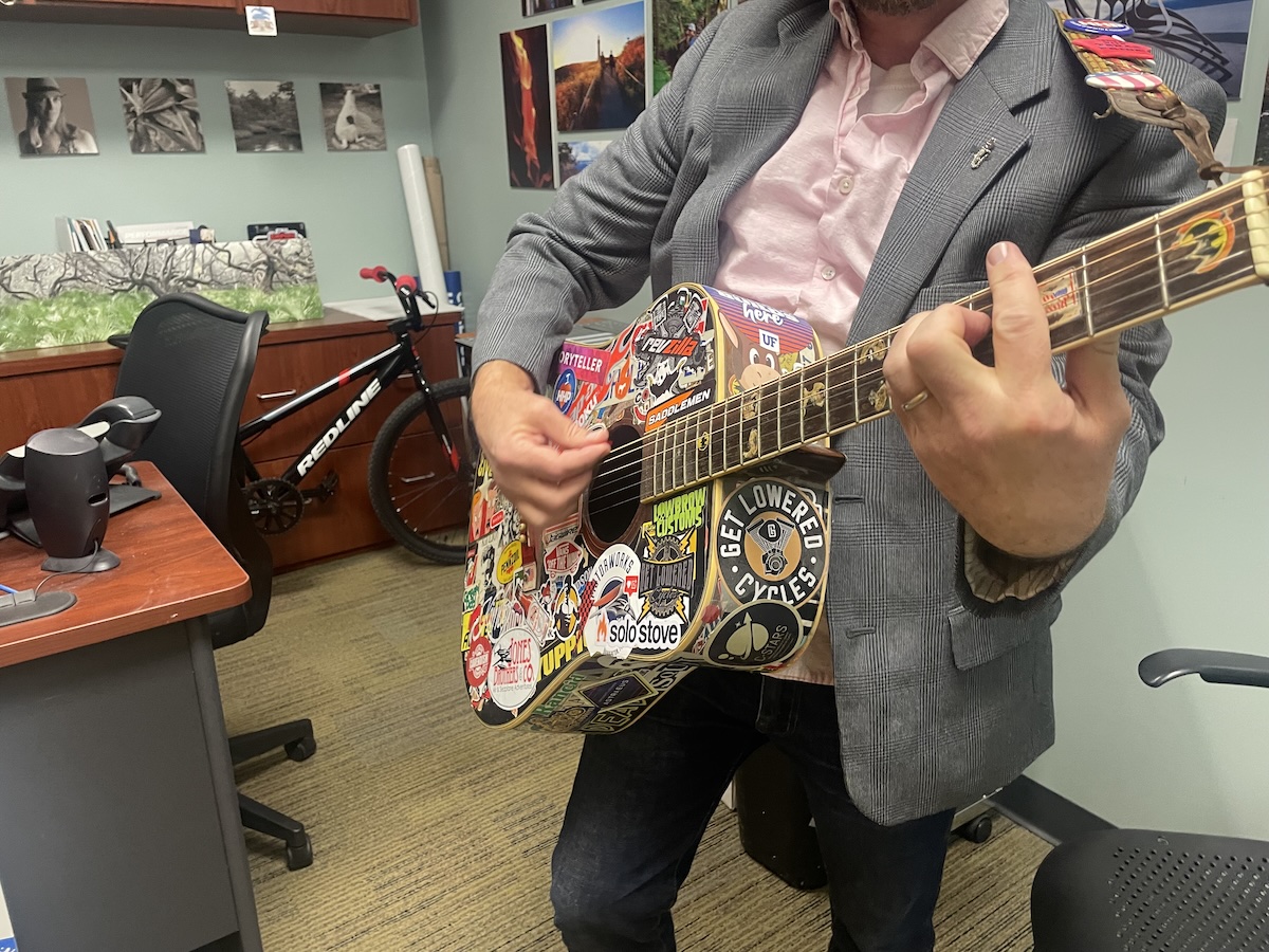 Coworker playing a guitar covered in bumper stickers in a nearly empty office