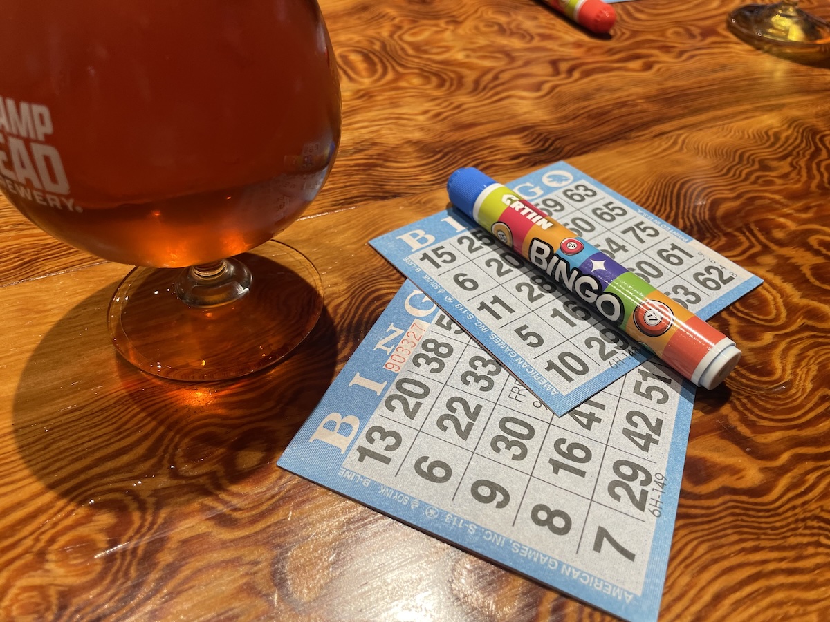Two blue bingo cards and a bingo marker on an amber wood table