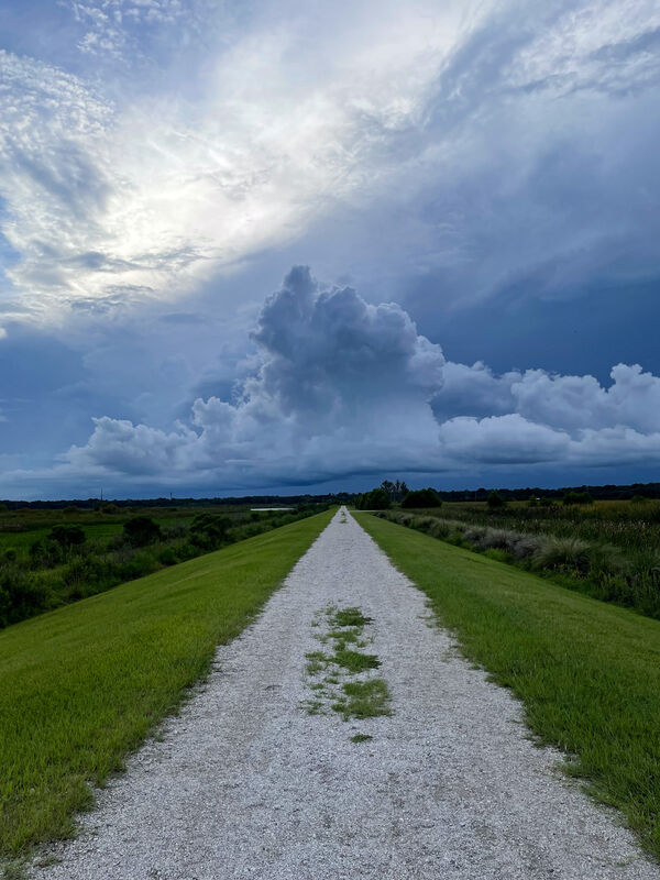 The walking path leading to large, stark clouds in the distance